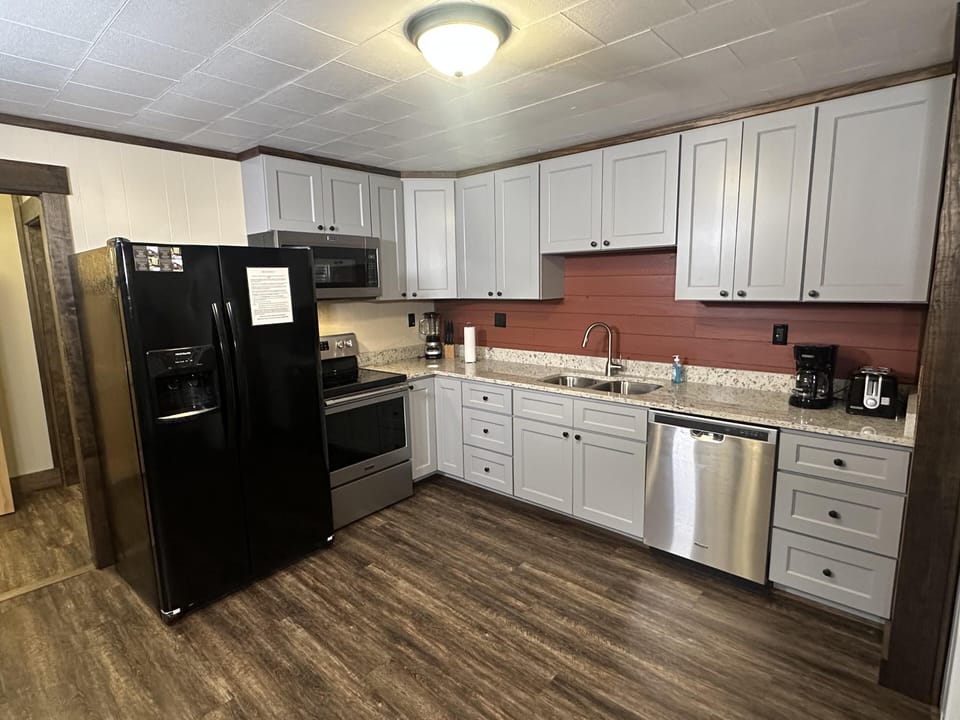 L-shaped kitchen with gray cabinets, granite countertops, stainless steel appliances, and a reddish wood plank backsplash.