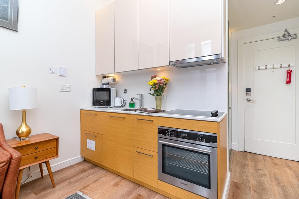 Compact kitchen with wood lower cabinets, white high-gloss upper cabinets, electric cooktop, and stainless steel oven.