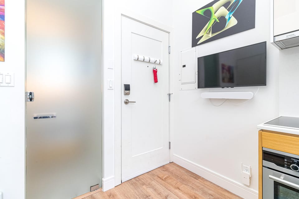 Entrance area with white door, frosted glass bathroom door, wall-mounted TV, and light wood flooring.