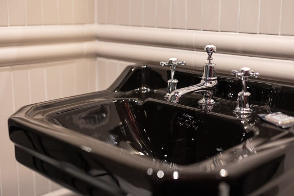Close-up of the black basin with traditional chrome taps and tiled wall.