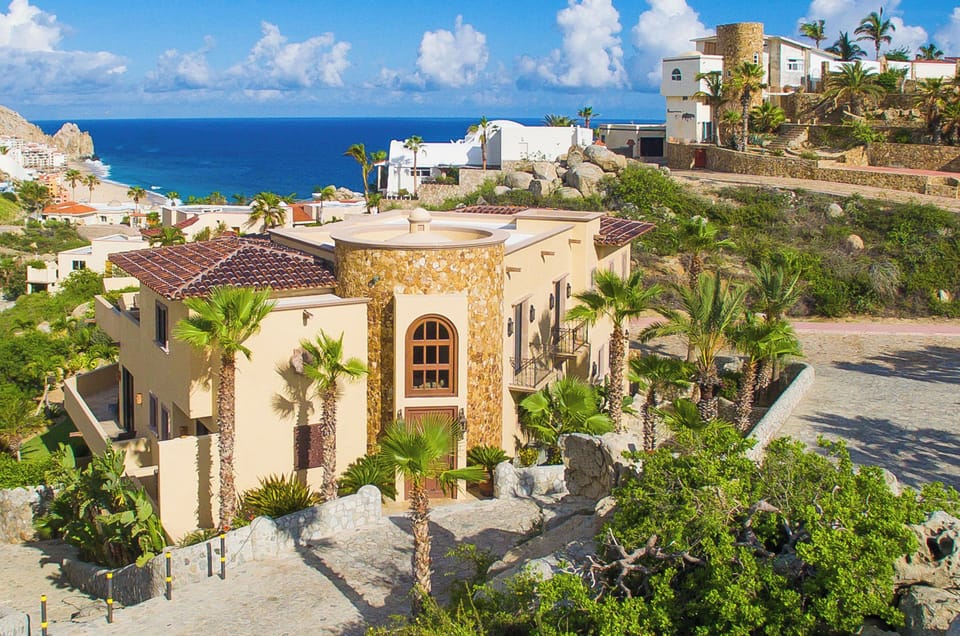 A stunning beachfront villa nestled among palm trees and natural landscaping, with sweeping ocean views and the sparkling Sea of Cortez beyond.