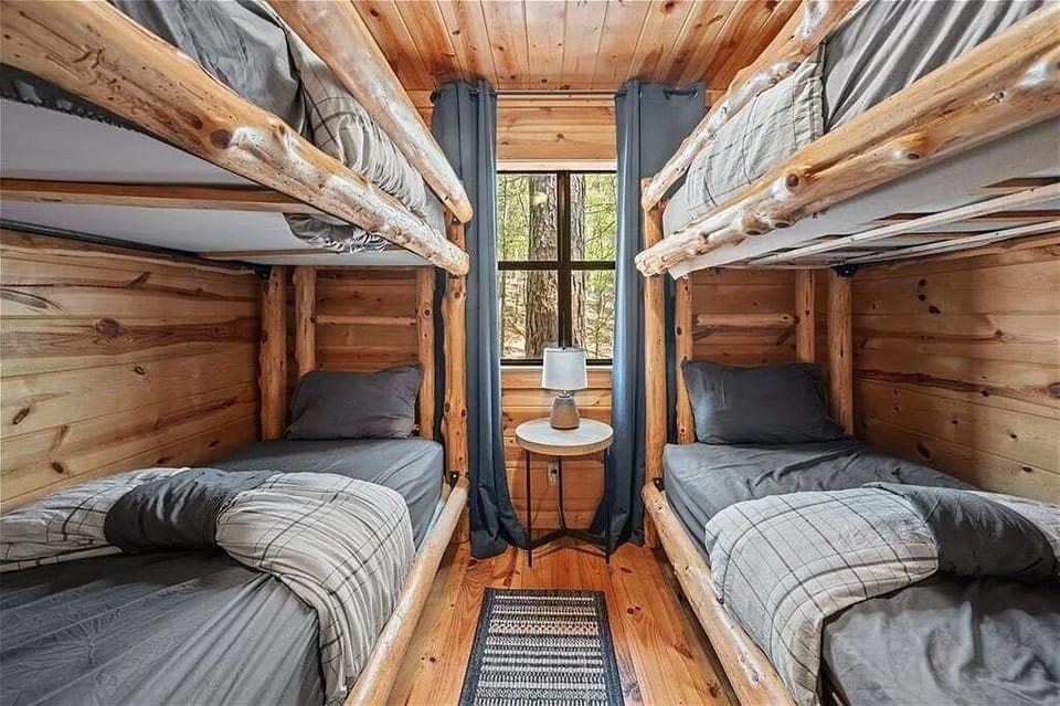 Cozy up in your rustic bunk room, where natural wood surrounds you and forest views peek through the window, perfect for groups or families seeking a charming retreat.