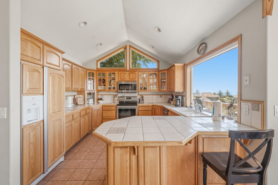 Picture yourself cooking in this bright, spacious kitchen with vaulted ceilings and stunning views. Ample oak cabinetry, modern appliances, and a large center island make meal prep a breeze.