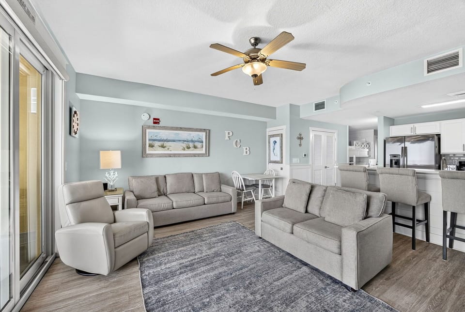 Settle into this bright, airy living space with calming coastal tones and plenty of room to unwind. Soft sofas, a gentle sea breeze from your balcony, and an open layout connecting you to the kitchen make this your perfect beach retreat.