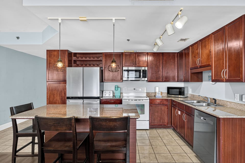 A fully equipped kitchen with rich wood cabinetry, stainless steel appliances, granite countertops, and a dining island awaits your culinary adventures and memorable meals together.