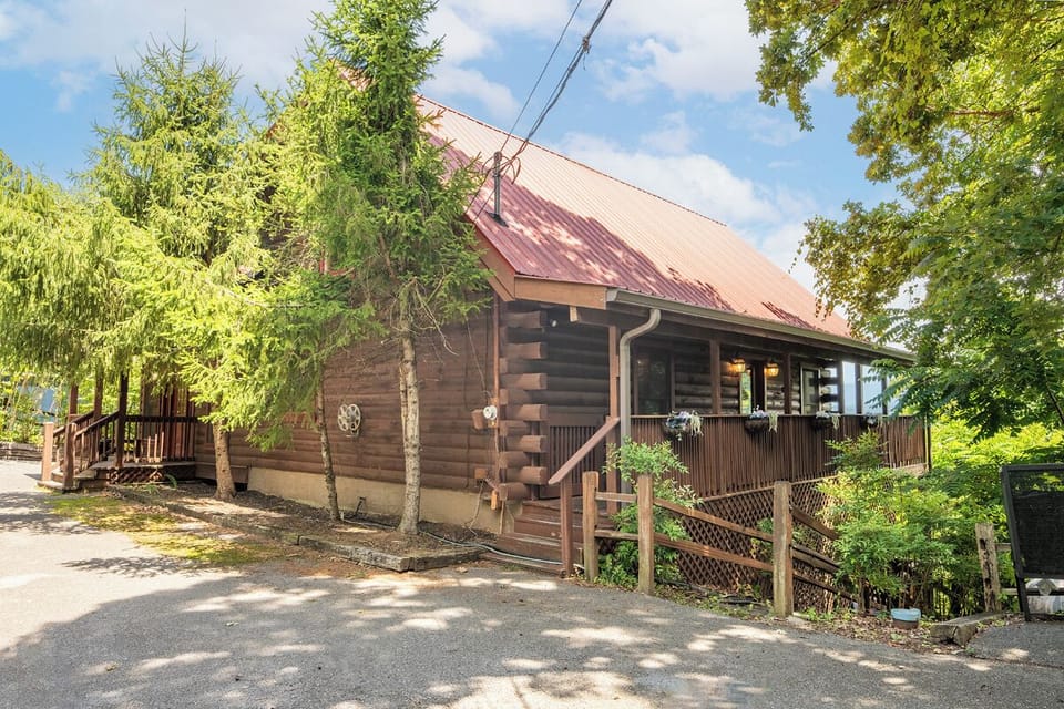 Charming log cabin with a rustic metal roof nestled among tall trees, offering a secluded mountain retreat with a welcoming front porch and easy parking access.