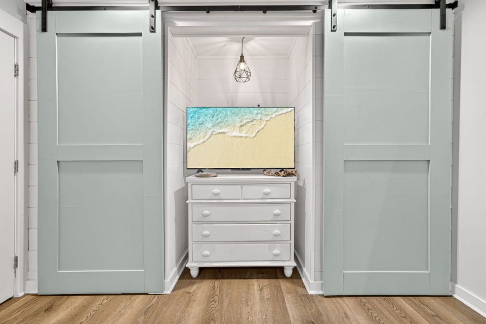 Slide open the charming barn doors to reveal your cozy bedroom nook with a wall-mounted TV and dresser—your perfect coastal retreat.