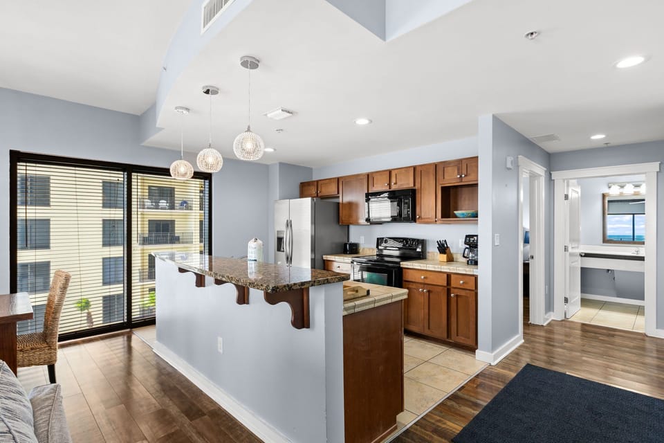Modern open-concept living with a fully equipped kitchen featuring granite countertops, stainless steel appliances, and elegant pendant lighting—your perfect home base for coastal adventures.
