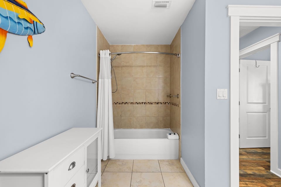 Your bathroom features soft blue walls, a clean tub-shower combo with decorative tiling, and thoughtful touches like playful wall art to brighten your daily routine.