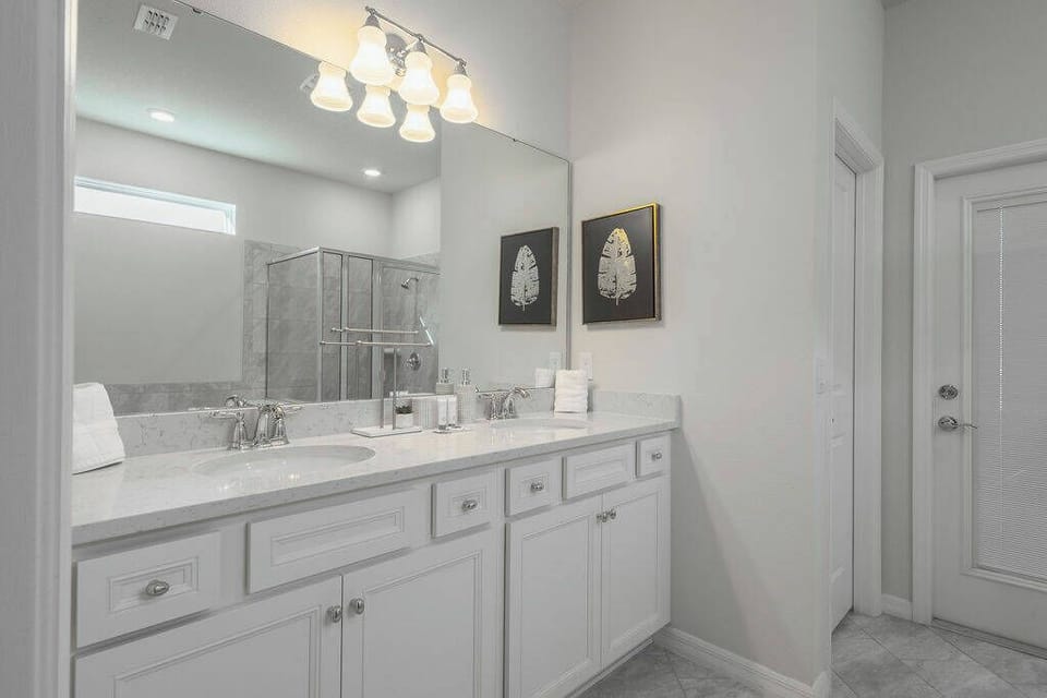 Enjoy a bright, airy bathroom with sleek white cabinetry and subtle gray tile, perfectly complementing the modern glass shower.