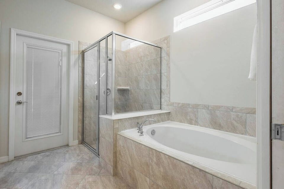 Experience a serene bathroom with elegant marble tiles and a spacious layout. The stylish glass shower complements the luxurious soaking tub, while natural light brightens the space, creating a perfect retreat for relaxation.