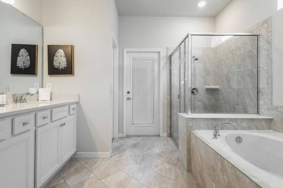 Relax in a beautifully designed bathroom with sleek white cabinetry and elegant stone accents. The spacious layout features a glass-enclosed shower and a luxurious soaking tub, perfect for unwinding after your day's adventures.
