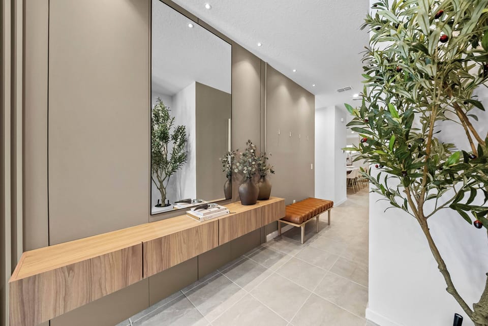 Welcome to a chic entryway featuring a sleek wooden console against warm beige walls. Natural light brightens the area, highlighting elegant decor and vibrant potted plants that bring a refreshing touch of nature inside.