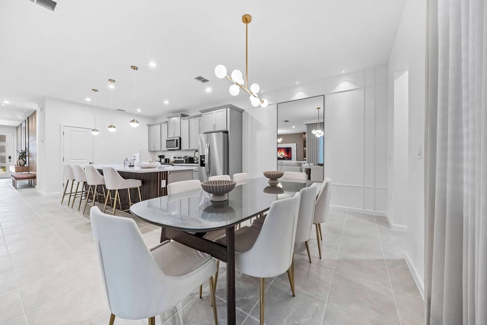 Experience a bright dining area with a sleek dark wood table and modern white chairs, ideal for family meals. The warm glow from stylish pendant lights creates a welcoming ambiance, seamlessly connecting to the kitchen.