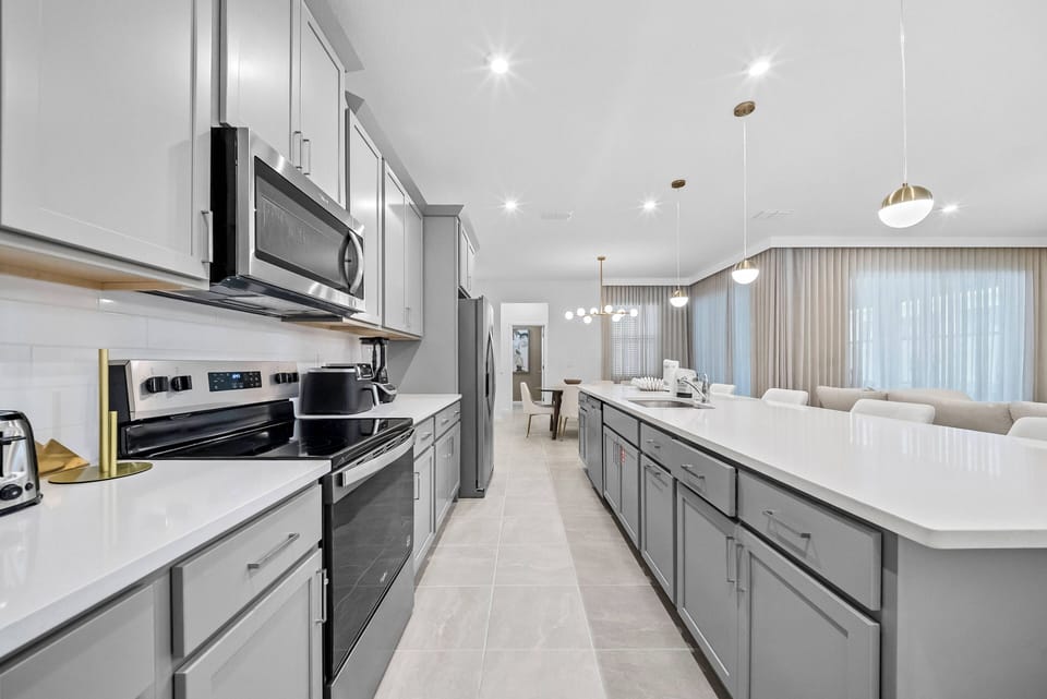 Step into a spacious kitchen where sleek gray cabinetry complements the bright, airy atmosphere. The large island invites gathering, while modern appliances and elegant lighting create a functional yet stylish culinary hub.