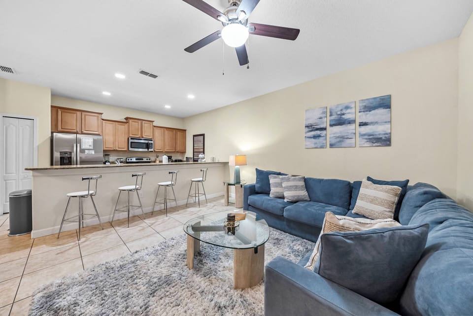 Unwind in the spacious living area with a plush blue sectional and sleek glass coffee table, flowing into a warm kitchen with modern appliances and vibrant artwork, making it the perfect spot to relax after your adventures.