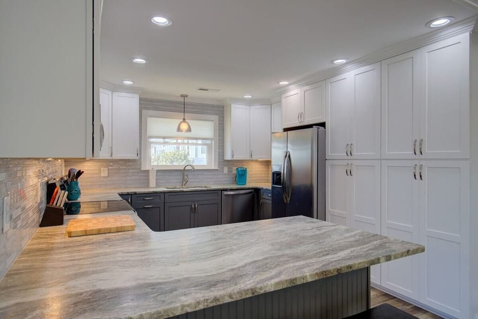 A modern kitchen with white cabinetry, a marble countertop, and a stainless steel refrigerator.
