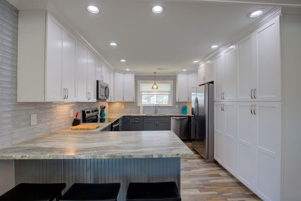 A modern kitchen with white cabinetry, a marble island, and recessed lighting.