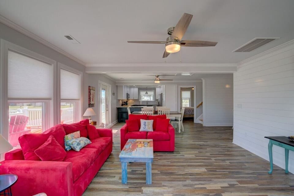 A spacious living room with red sofas, a wooden floor, and a ceiling fan.