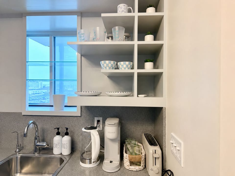 Bright kitchenette with coffee station, open shelving, and city-view window
