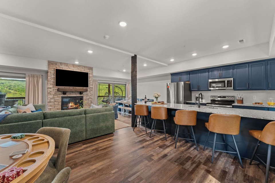 Gather in the bright, open-concept living and kitchen with a green sectional, stone gas fireplace, and a navy island that seats the whole group.