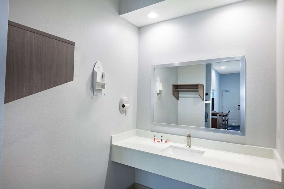 Clean sink area with mirror, counter, and wall shelf