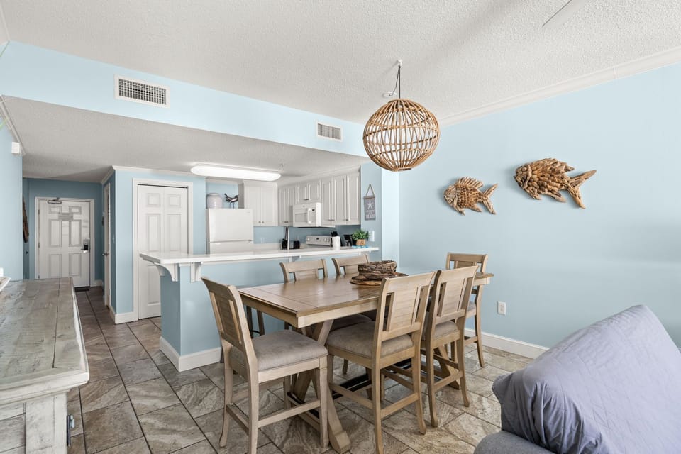 Dining area with wooden table and coastal decor adjacent to a light blue kitchen.