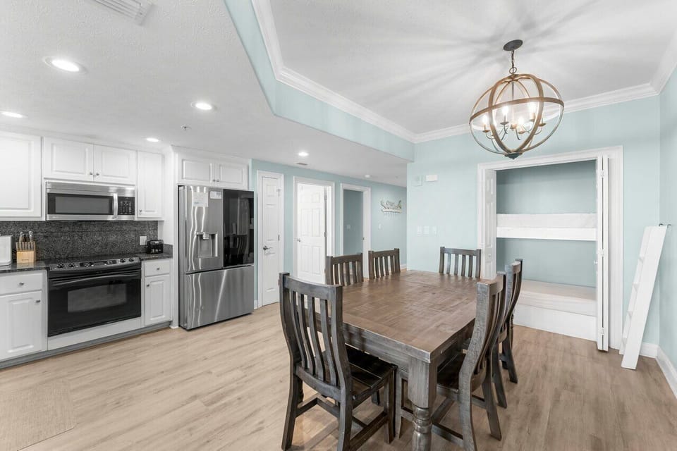 Your open-concept dining and kitchen area blends coastal charm with modern convenience, featuring a welcoming farmhouse table perfect for gathering over meals and memories.