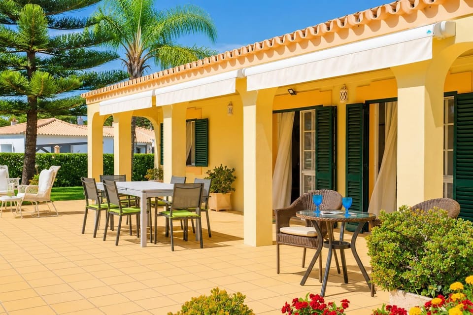 Wide-angle view of a sunny villa backyard featuring a swimming pool, lounge chairs, and a large green lawn.