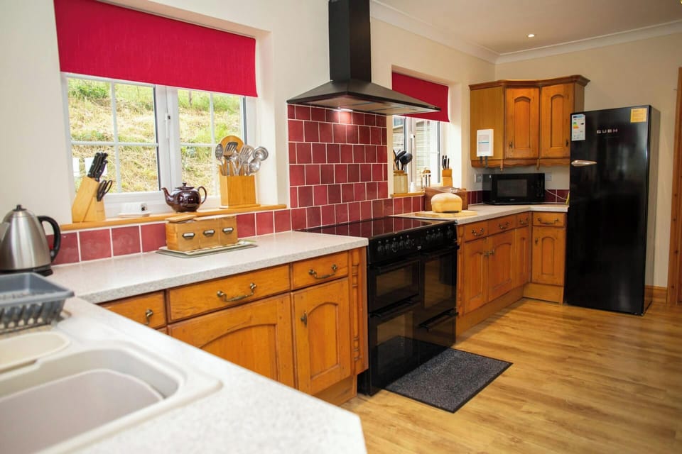 Traditional wooden kitchen with black cooker and extractor hood, red tiled splashback and red blind