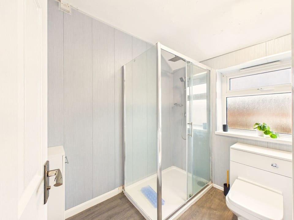 Enjoy a clean, functional layout with light blue paneled walls, stylish wood-effect flooring, and plenty of natural light from the frosted privacy window.