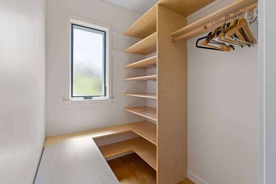 Primary bedroom custom built-in shelving and hanging space in a sunlit walk-in closet.
