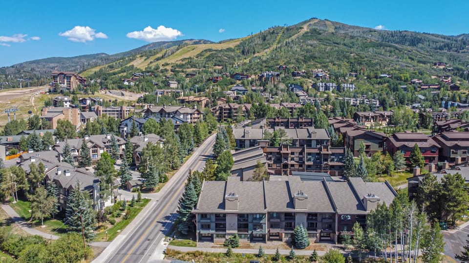 Aerial view of a mountain resort community nestled among evergreen trees and rolling peaks, with ski slopes visible in the distance.