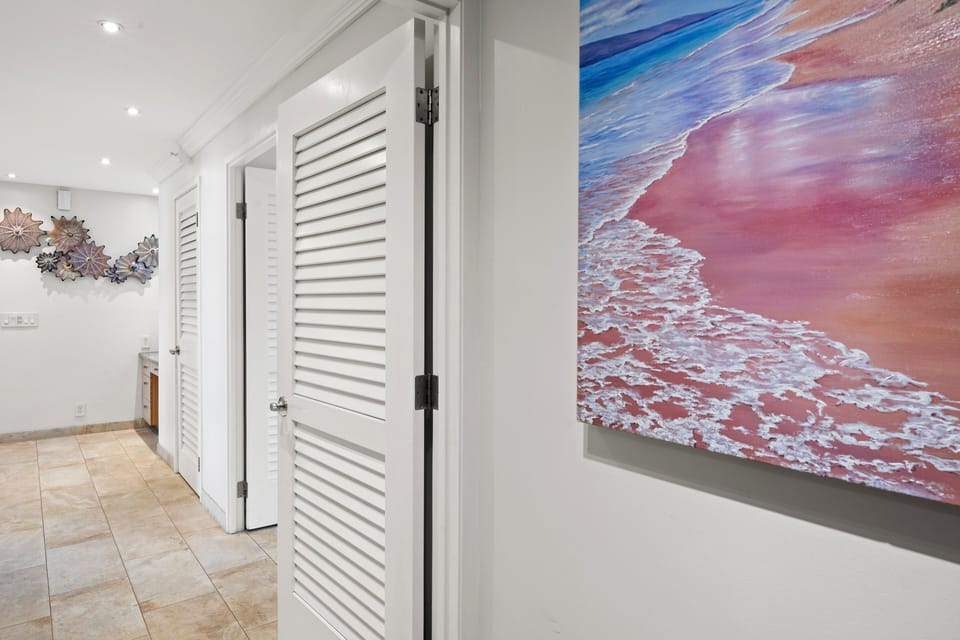 A bright hallway featuring clean white lines, custom louvered doors, and a vibrant tropical beach canvas.