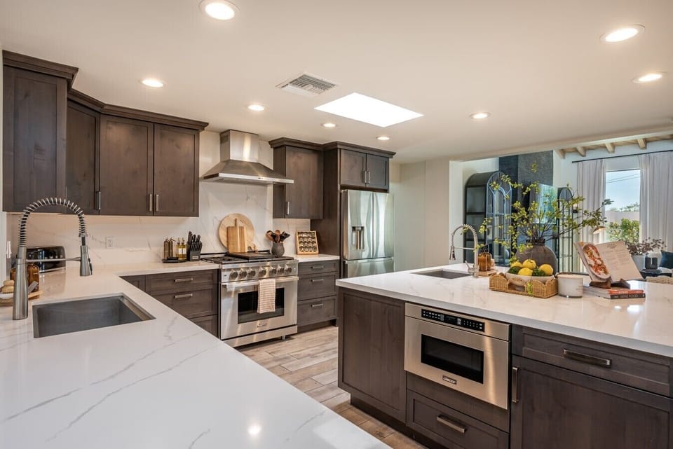 A modern kitchen with dark cabinetry, stainless steel appliances, and quartz countertops.