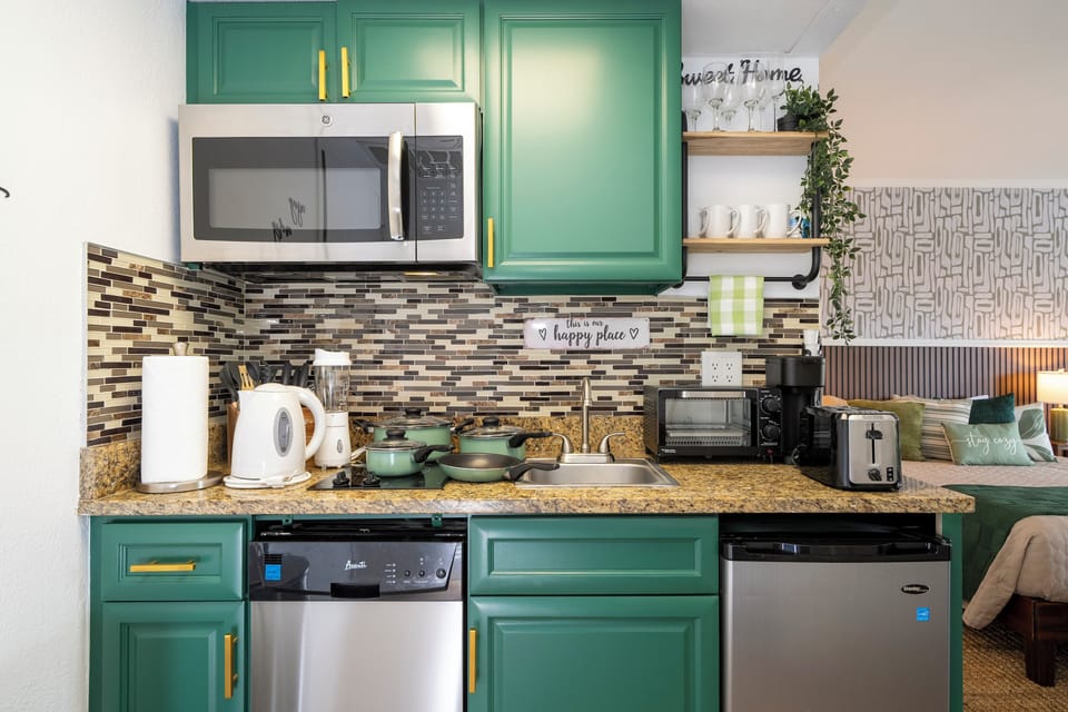 Cook with ease in a stylish, fully equipped kitchenette designed for comfort and convenience. Featuring modern cabinetry, a cooktop, microwave, dishwasher, mini fridge, sink, coffee maker, cookware, dishes, glasses, utensils, and ample counter space.