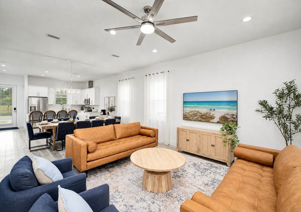 1st Floor - Bright open-concept living room with comfortable group seating, a 75-inch 4K Smart TV, and easy flow to the kitchen and dining area—perfect for relaxing together after the beach.