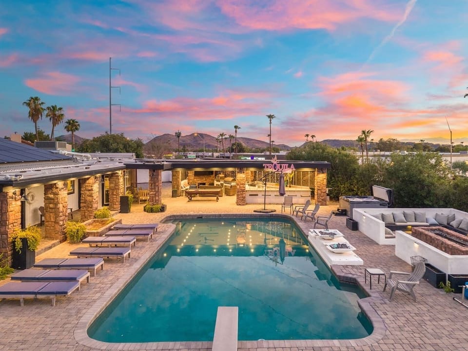 Loungers line the pool as a purple-pink sunset stretches over the covered patio bar and lounge area.