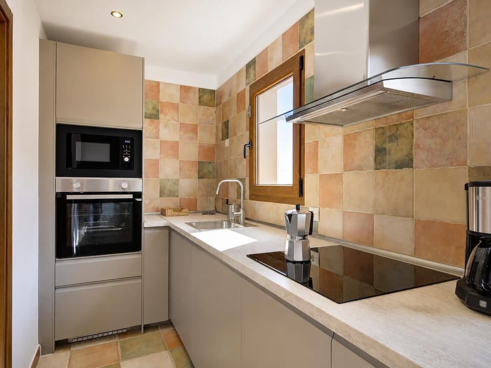 Modern fully-equipped galley kitchen featuring integrated grey cabinetry, a built-in oven and microwave, a sleek induction cooktop, and rustic tiled splashbacks.
