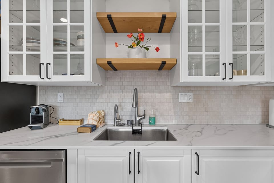 Step into a bright, modern kitchen where marble countertops meet crisp white cabinetry and warm wood shelving. You'll love preparing meals here, with a coffee maker ready for your mornings.