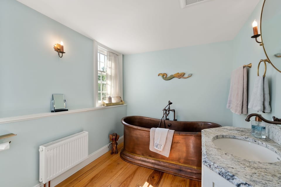 Bathroom featuring a copper soaking tub, vanity, and light wood flooring.