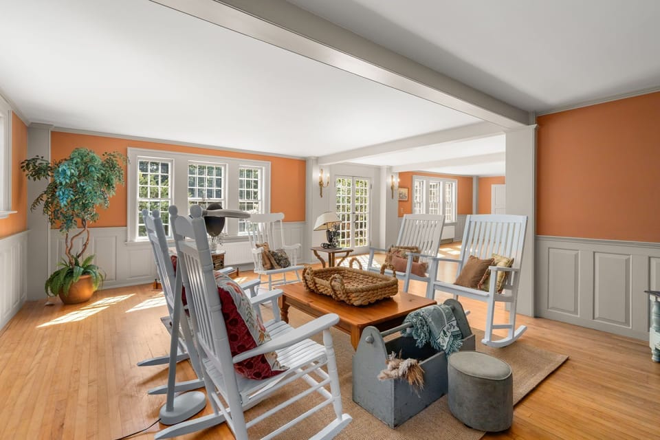Living space featuring terracotta walls, grey wainscoting, and white rocking chairs.