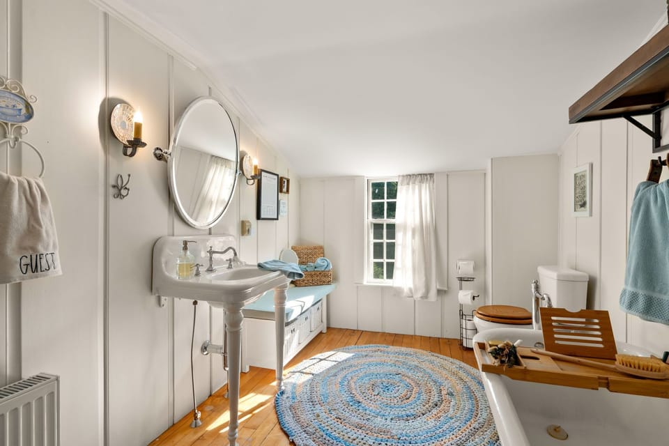Cottage-style bathroom with a vintage sink, soaking tub, and wood floors.
