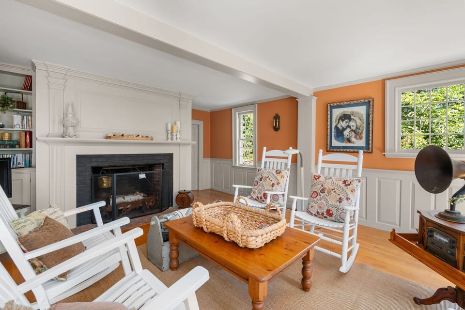 Living room with a brick fireplace, white rocking chairs, and burnt-orange accent walls.