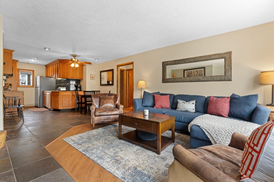 Settle into your inviting open-concept living space, where a plush blue sectional and warm wood accents create the perfect spot to unwind after exploring. Your fully equipped kitchen awaits your home-cooked meals.