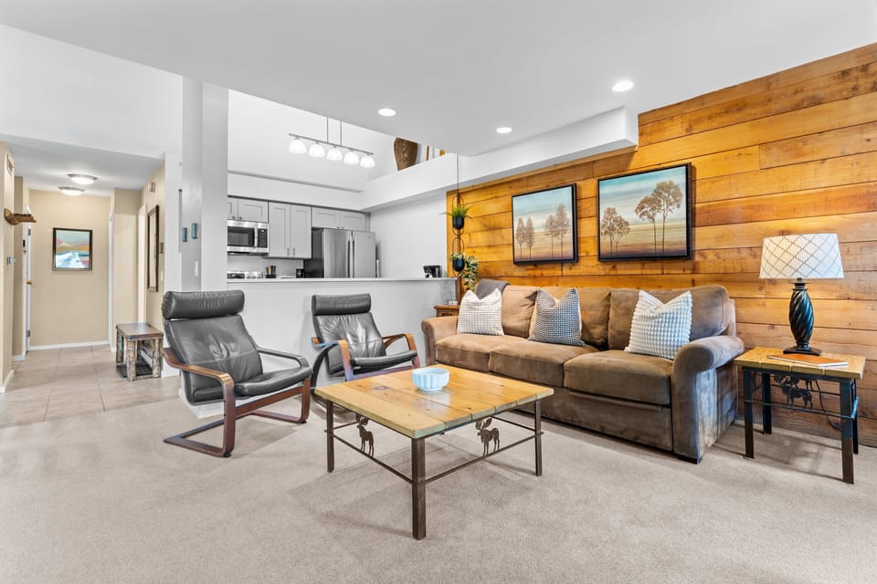 Your spacious living room features a warm wood accent wall, plush leather seating, and an open kitchen design that invites relaxation and togetherness after your daily adventures.