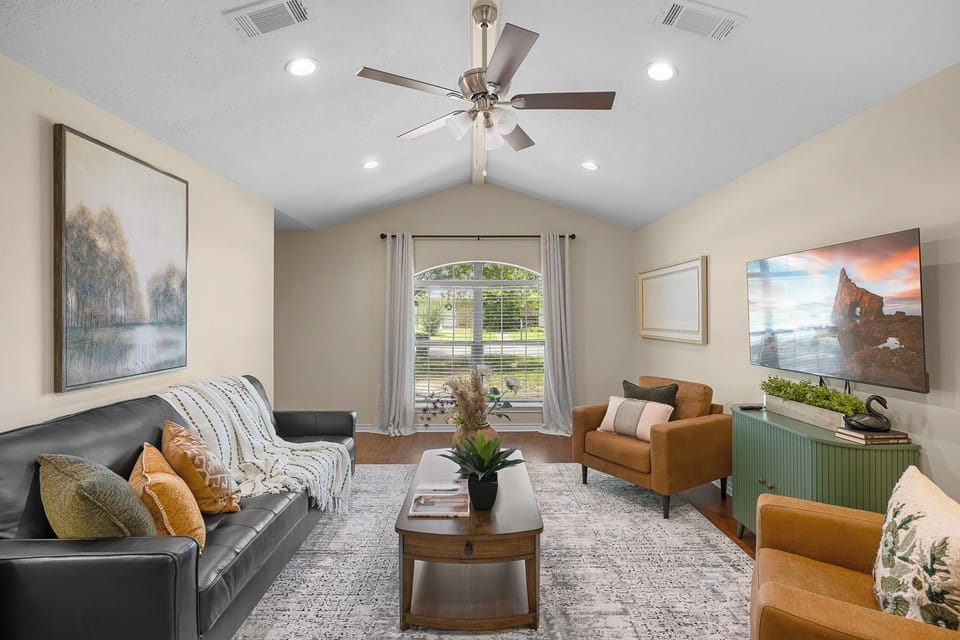 Bright vaulted living room with cozy seating, big window, and TV