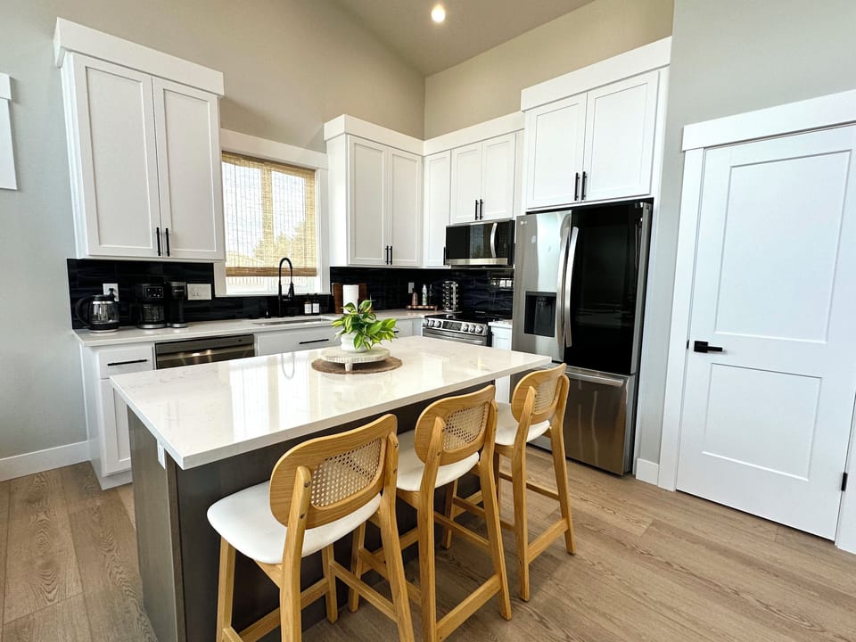 The kitchen sits just off the great room — white quartz counters, full-size stainless appliances and island seating for three. Bring your clothes and your groceries; we have the rest.