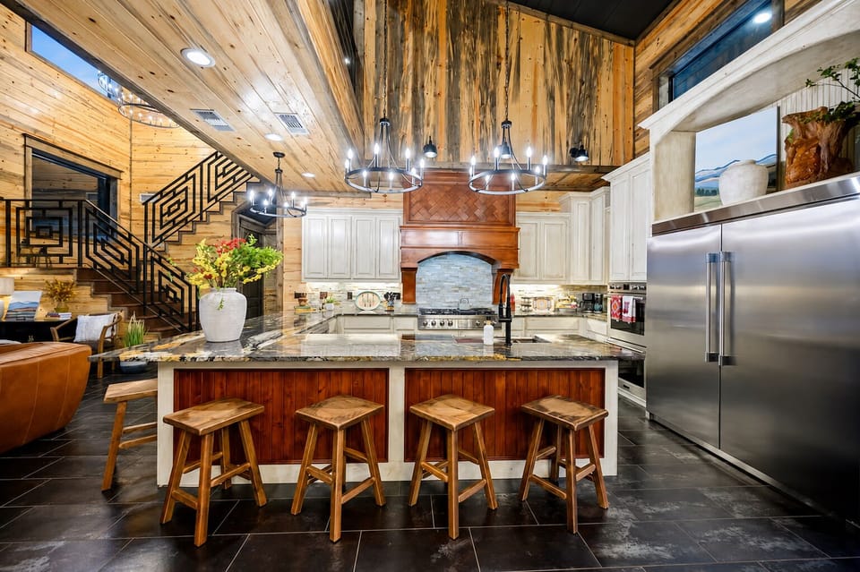 Large kitchen with an oversized island, bar seating, stainless steel refrigerator, custom cabinetry, pendant lighting, and open access to the living area.