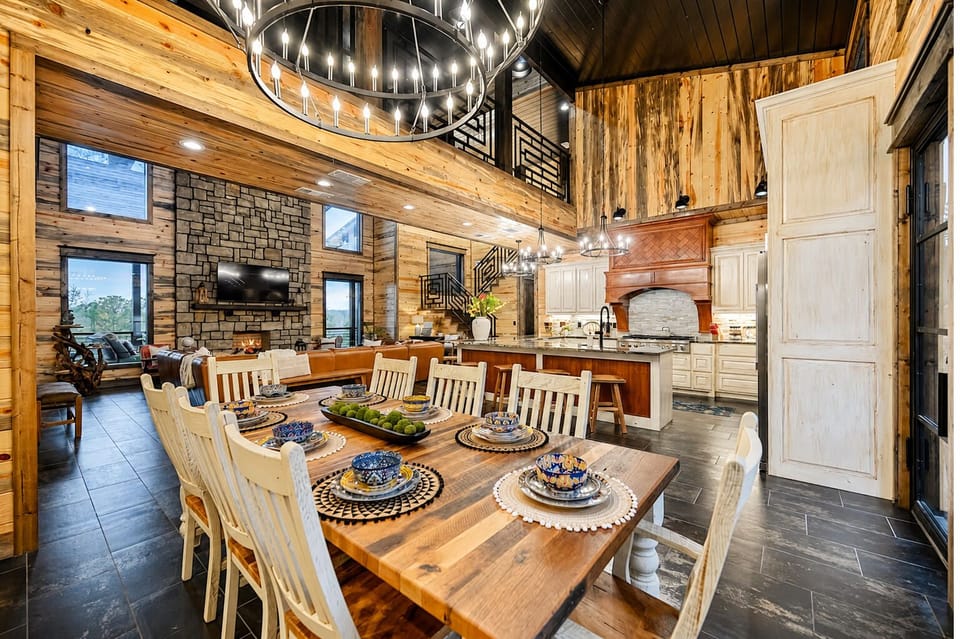Spacious dining area with a large wood table, group seating, rustic chandelier, and open flow to the kitchen and living room.